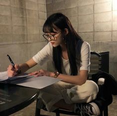 a woman sitting at a table writing on a piece of paper with a pen in her hand