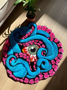 a blue and pink rug with an evil eye on it next to a potted plant