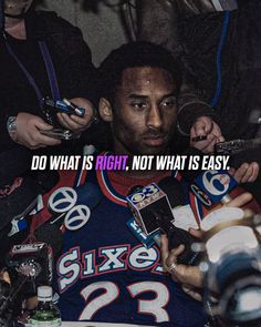 a man in a blue jersey surrounded by reporters holding cell phones and talking on the phone