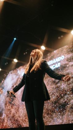 a woman standing in front of a large screen with her hands out to the side