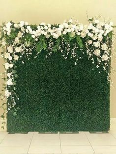 an artificial hedge wall with white flowers and greenery on the top, in front of a tiled floor