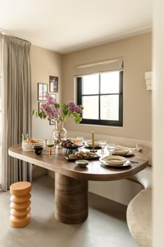 a dining room table with plates, bowls and flowers on it in front of a window