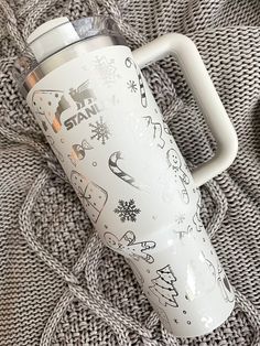 a white coffee mug with drawings on it sitting on a gray knitted surface next to a cup holder