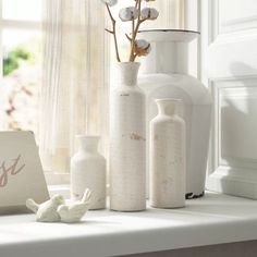 white vases with flowers in them sitting on a window sill next to a sign