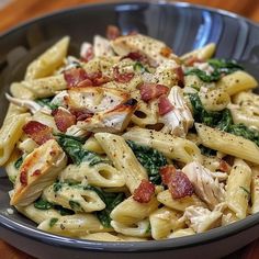 a pasta dish with chicken, spinach and bacon in a bowl on a wooden table