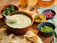 a wooden table topped with bowls filled with dip and tortilla chips next to beer