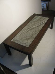 a wooden table with marble top sitting on a white floor in front of a wall