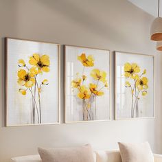 three yellow flowers are hanging on the wall above a white couch in a living room