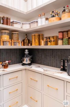 a kitchen with white cabinets and shelves filled with jars, containers and other items on the counter