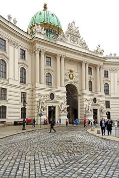 people are walking around in front of a large white building with a green dome on top