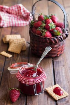 strawberry jam in a jar with crackers and strawberries next to it on a wooden table