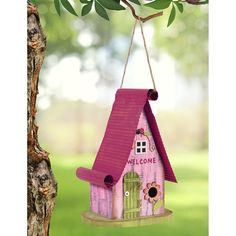 a pink birdhouse hanging from a tree in the grass with a welcome sign on it