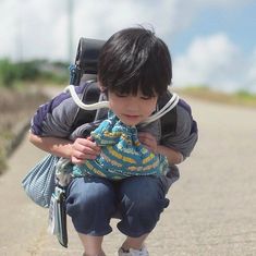 a little boy kneeling down to pick up something off the ground while wearing a backpack