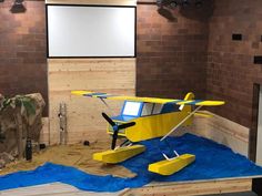 a small yellow airplane sitting on top of a blue tarp in front of a projector screen