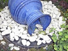 a large blue barrel sitting on top of a pile of rocks next to some plants