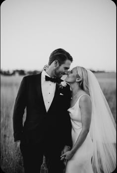 a bride and groom kissing in the middle of a field with tall grass behind them