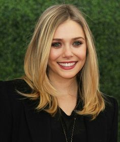 a woman with blonde hair wearing a black suit and smiling at the camera while standing in front of a green wall