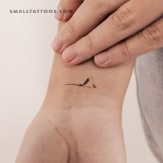 a small bird tattoo on the wrist is shown in black ink, while someone's hand holds it