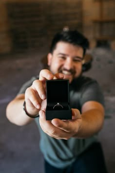 a man holding a ring in his right hand and pointing it at the camera while smiling