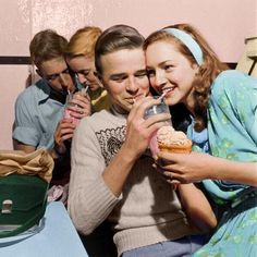 two women and one man are sitting together drinking milk from a bottle while the other woman is holding a cupcake