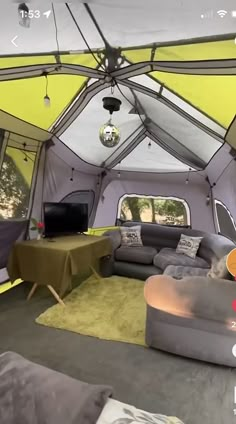 the inside of a tent with couches, tables and television in it's center