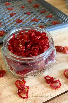 a glass jar filled with dried red peppers on top of a wooden cutting board next to a grate