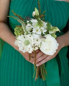 a woman in a green dress holding a bouquet of white flowers and greenery on her arm