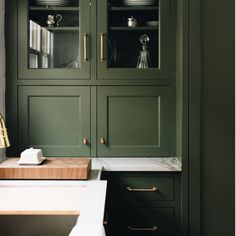 a kitchen with green cabinetry and marble counter tops, gold pulls on the handles