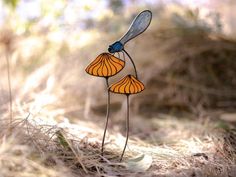 two stained glass flowers in the grass with a blue dragonfly sitting on top of them