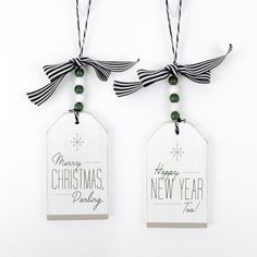 two white tags with black ribbon and green beads hanging from the top of each tag