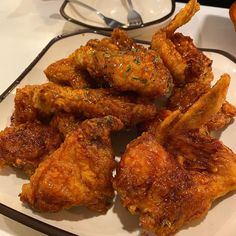 fried chicken wings on a white plate with utensils in the backgroud