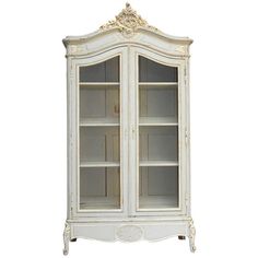 a white china cabinet with glass doors and gold trimmings on the bottom shelf