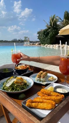 a table with plates of food and drinks on it next to the water at a resort