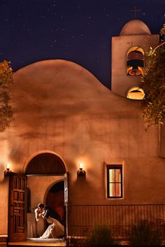 a bride and groom standing in front of a church at night with the stars above them