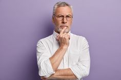 an older man wearing glasses and a white shirt is posing with his hand on his chin