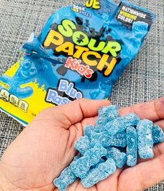 a hand holding blue raspberries next to a bag of gummy bear bears