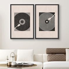 two framed records are hanging on the wall above a white couch in a modern living room