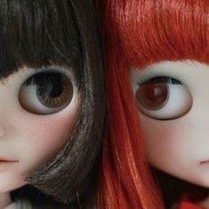 two dolls, one with red hair and the other with brown eyes are posed side by side