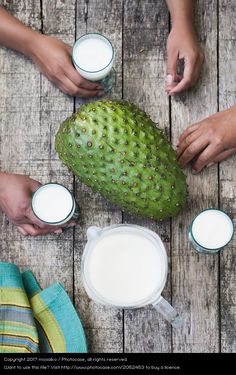 three people are holding glasses with milk and an unripe fruit on the table