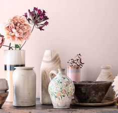 various vases and bowls are arranged on a table with flowers in the background,