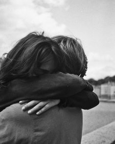 black and white photograph of two people hugging each other on the side of the road