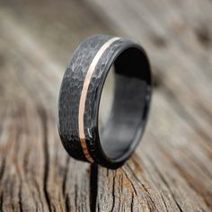 a black ring with gold inlays sits on a wooden surface