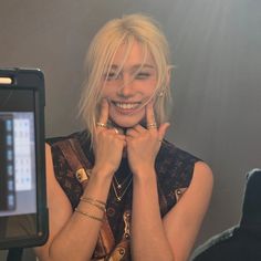 a woman with blonde hair smiling in front of a mirror and holding her hands to her face