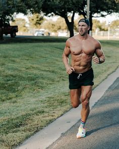 a shirtless man running down the street in shorts and no shirt, with trees in the background