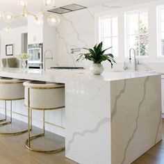 a white kitchen with marble counter tops and stools next to an island in the middle