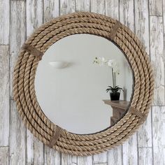 a round rope mirror hanging on the wall next to a table with a potted plant