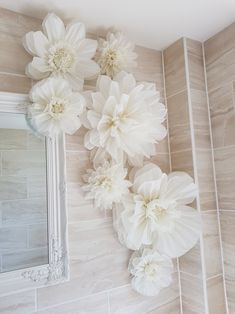 white paper flowers are hanging on the wall next to a mirror and tiled walls in a bathroom