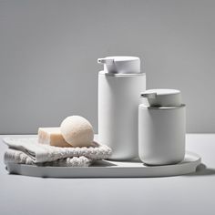 three white containers sitting on top of a table next to a towel and soap dispenser