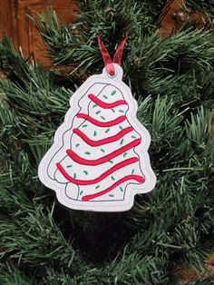 a christmas tree ornament hanging from a pine tree with red and green ribbon