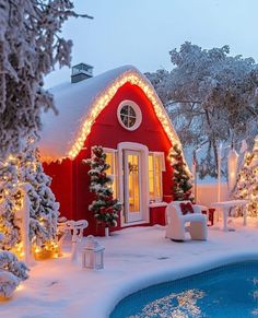 a red house covered in christmas lights next to a swimming pool and tree lined with snow